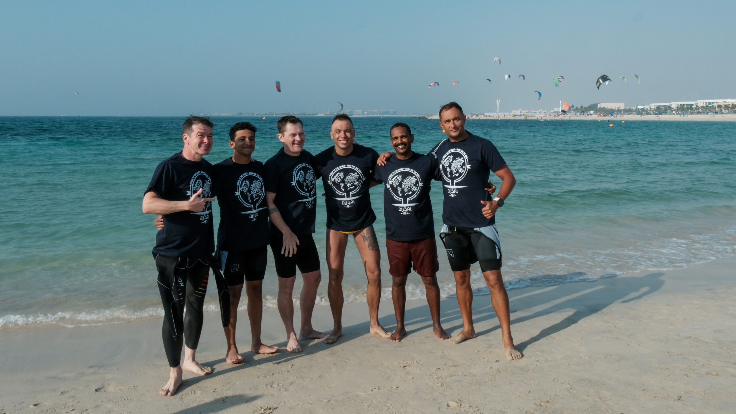 Group of men in black outfits posing on Dubai beach by the water.